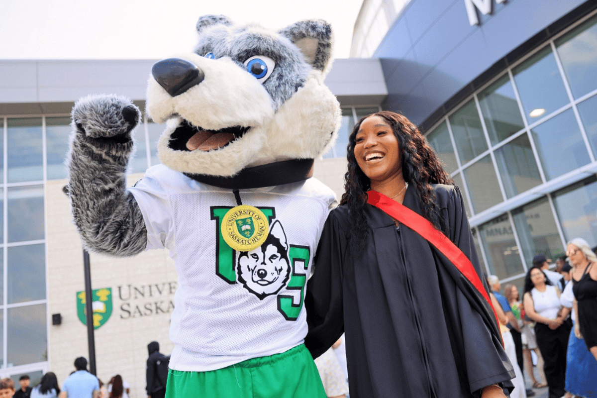 A student in convocation attire posing with Howler.