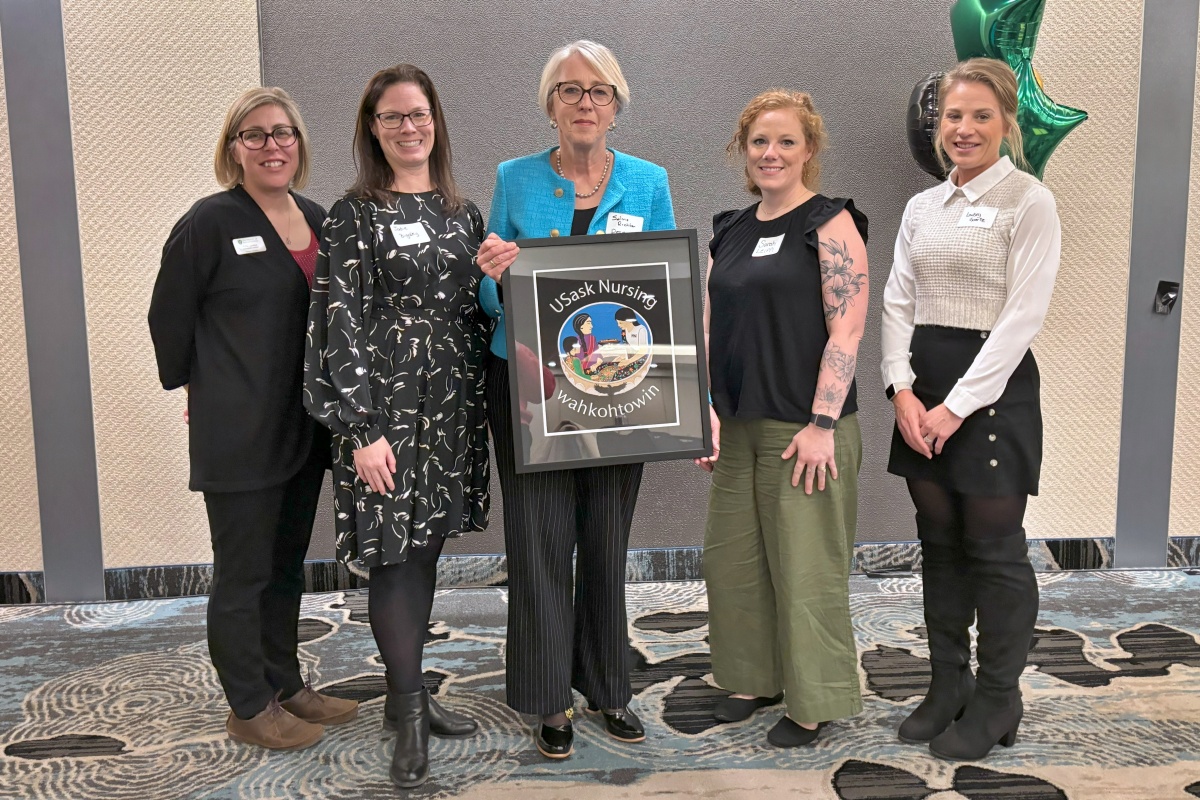 Solina Richter holding a piece of art that says USask Nursing wahkohtowin, standing between four women
