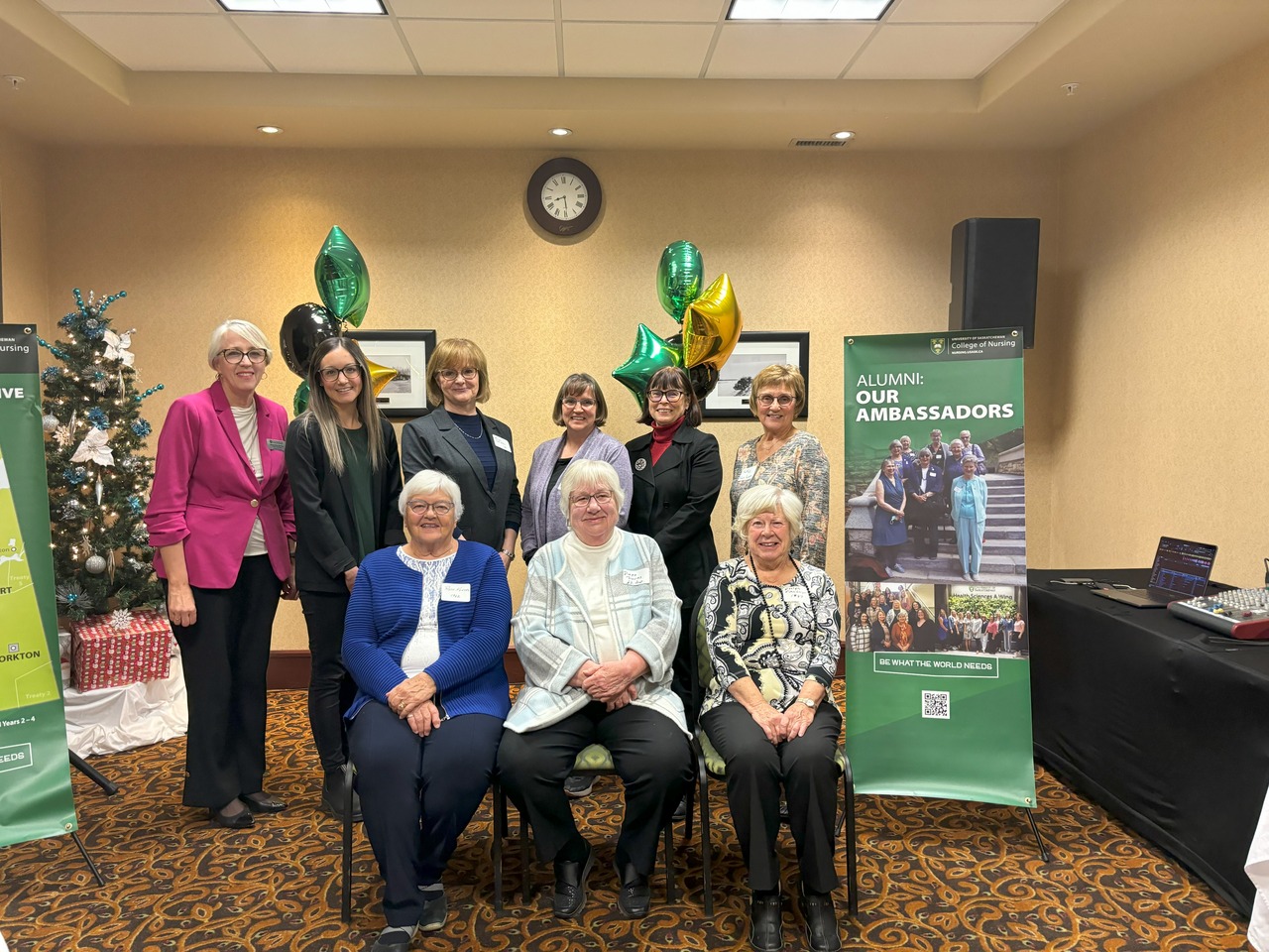 three women sitting on chairs in front of six standing women standing inbetween two College of Nursing banners