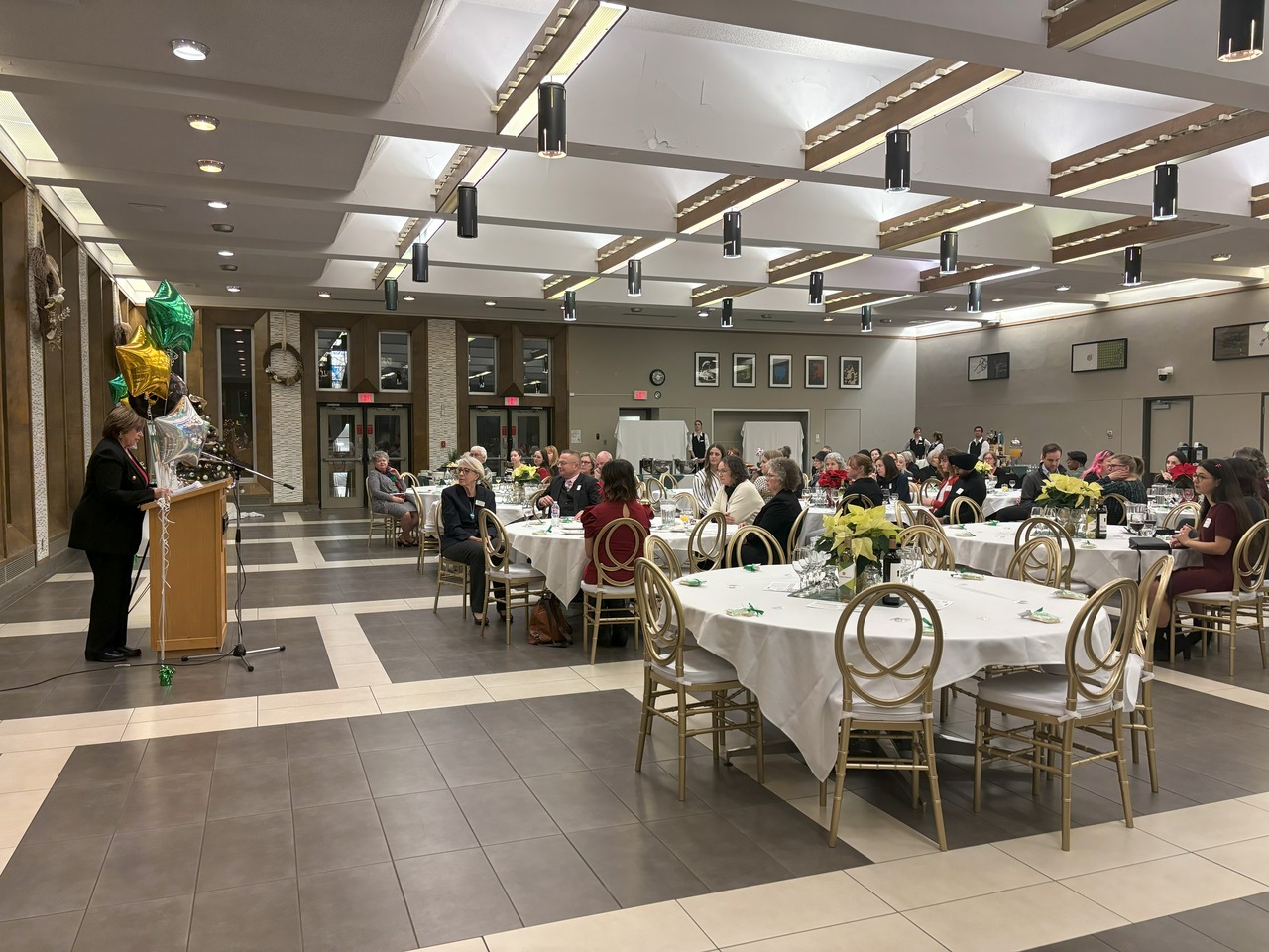 a woman speaking to a crowd of people seated at circular tables
