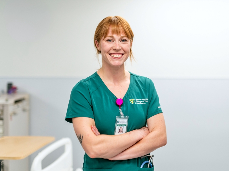 Female student in green nursing scrubs stands in front of camera.