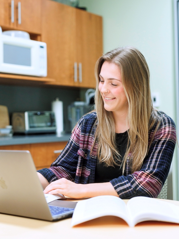 Female student studying with a computer and textbook in a kitchen.