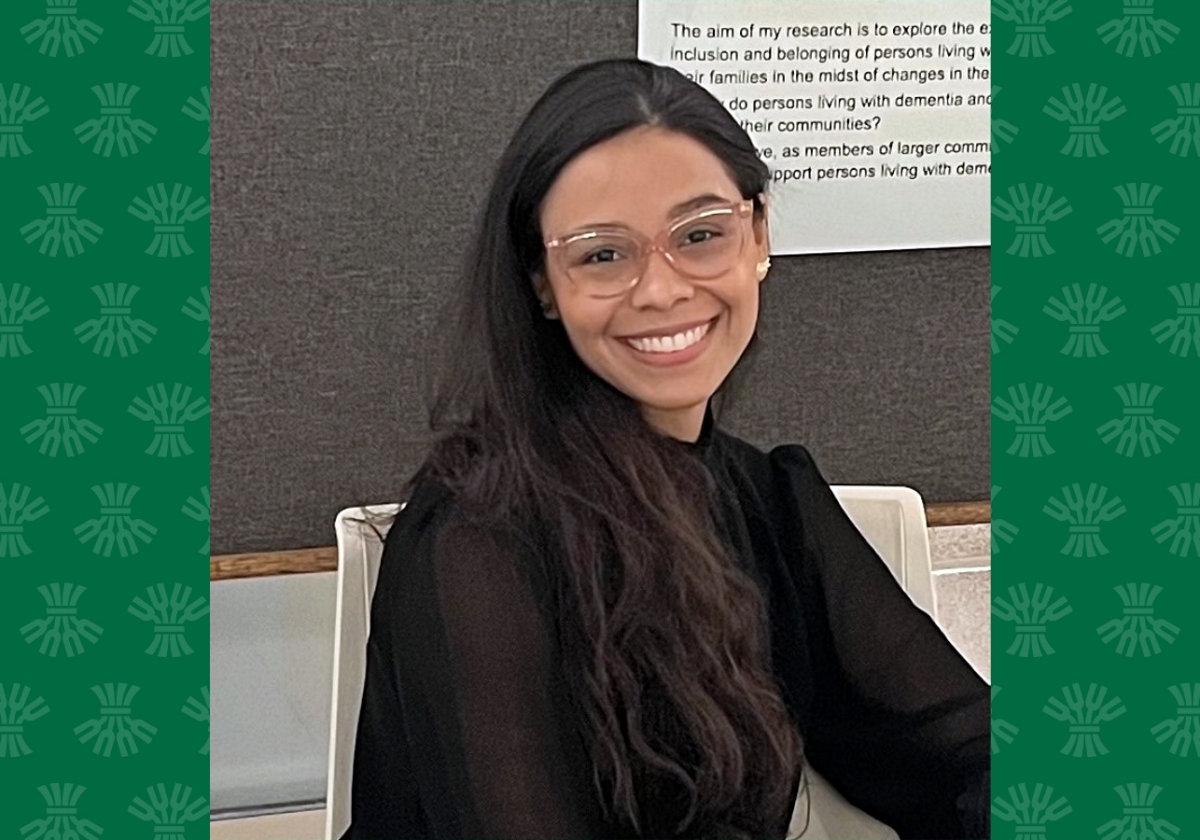 Female student sits smiling for the camera with green University of Saskatchewan branding in the background. 